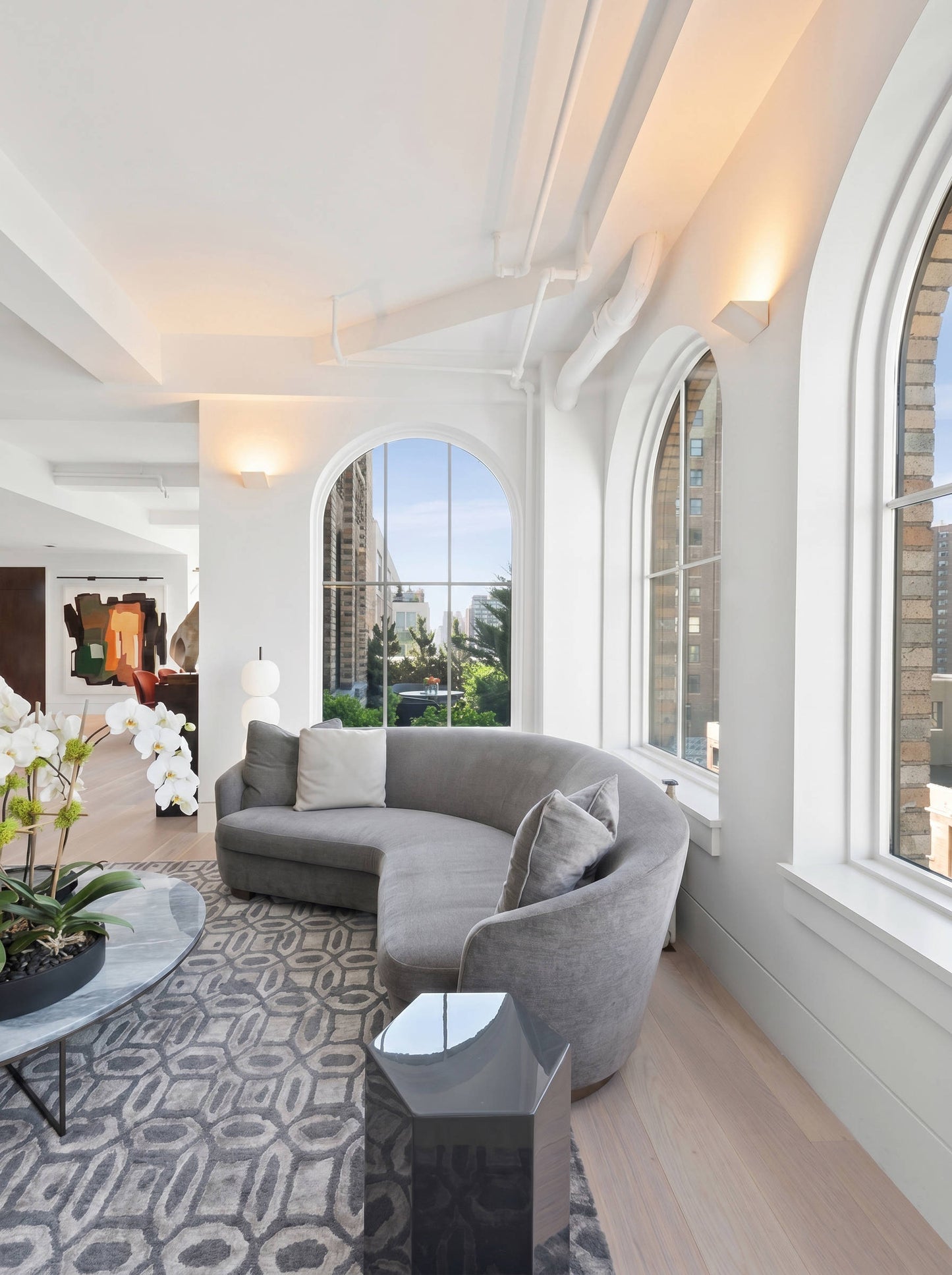 Modern living room with a curved gray sofa, large windows, and decorative elements. Point Sconces are on the left and facing walls.